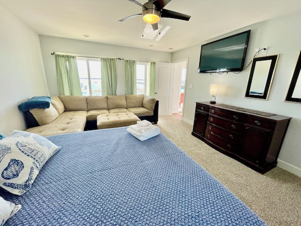 A bedroom with a bed, a sofa, a dresser, a television, and a window with curtains.