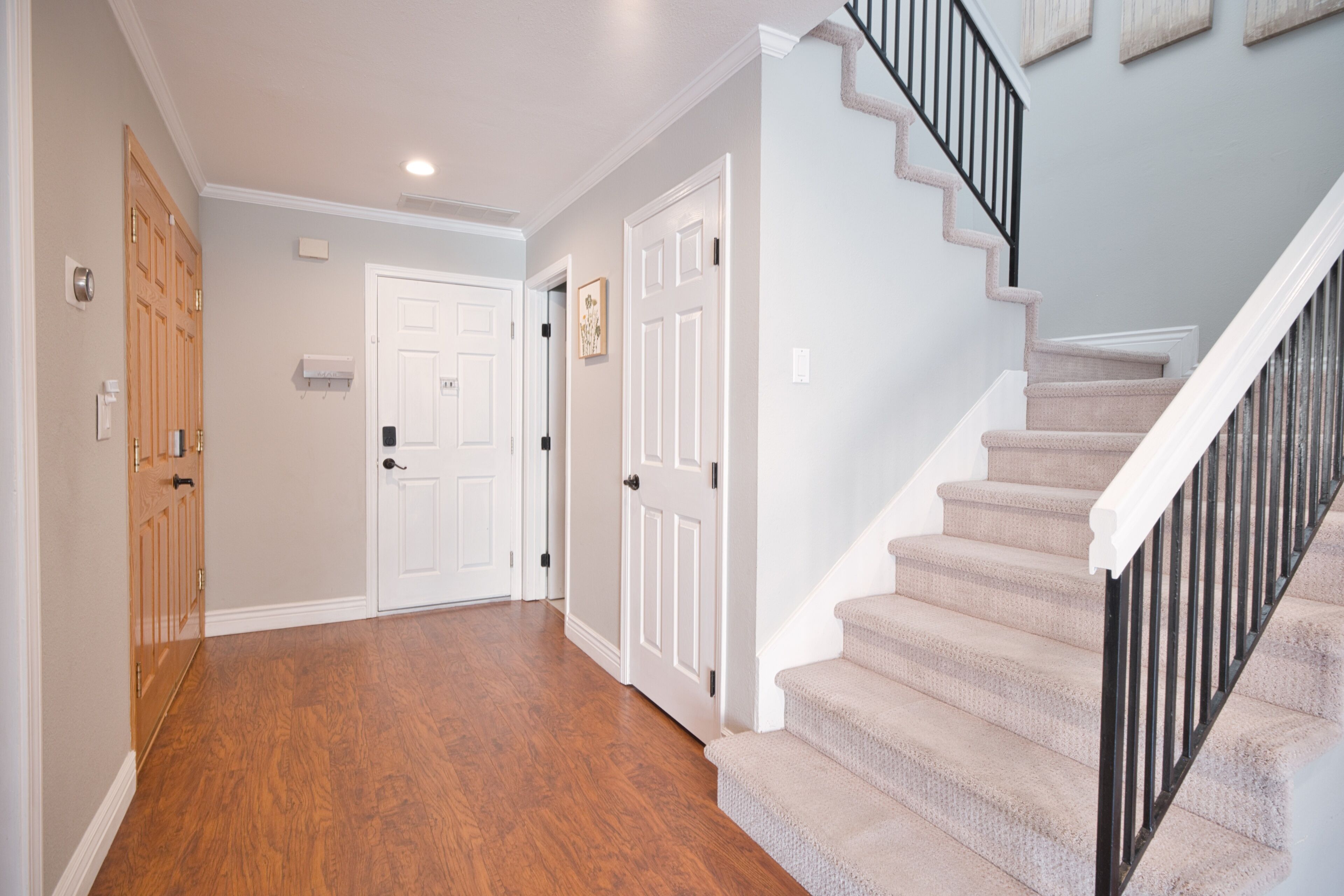 A hallway with wooden flooring, white doors, and a carpeted staircase with black railings.