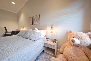 Ein Schlafzimmer mit einem Bett, Nachttischen, einer Lampe, einem Teddybären und Wandbildern.