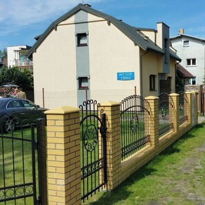 A building with a beige exterior, a blue sign, and a black metal fence. - Lazy Morze Mielno/uniescie (gmina Sianów)