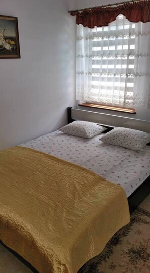 A single bed with a yellow bedspread, two pillows, and a window with lace curtains. - Lazy Morze Mielno/uniescie (gmina Sianów)