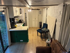 Eine kleine Küche mit Spüle, Mikrowelle und Kaffeemaschine. Es gibt einen Essbereich mit Stuhl und Tisch, sowie eine kleine Sitzecke mit einer Couch.