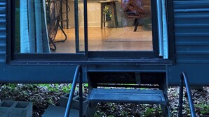 Ett rum med en skjutdörr av glas, ett litet bord med en växt, en stol och ett fönster med gardiner.