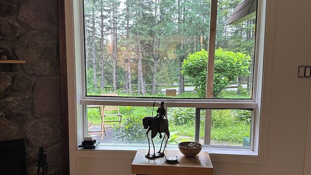 Una habitación con un ventanal grande, una pared de piedra, una mesa de madera con una escultura y una chimenea.