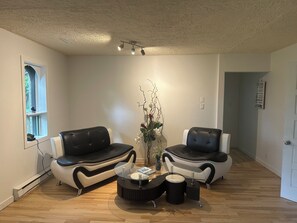 A modern living room with two black leather sofas, a glass coffee table, and a decorative plant.