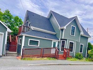 A two-story house with a steeply pitched roof, a front porch, and a fenced yard.