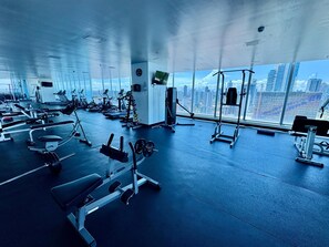 A gym with various exercise equipment, large windows, and a view of a cityscape. - Oceanview 1BR, Avenida Balboa, Steps to Cinta Costera (Panamá)