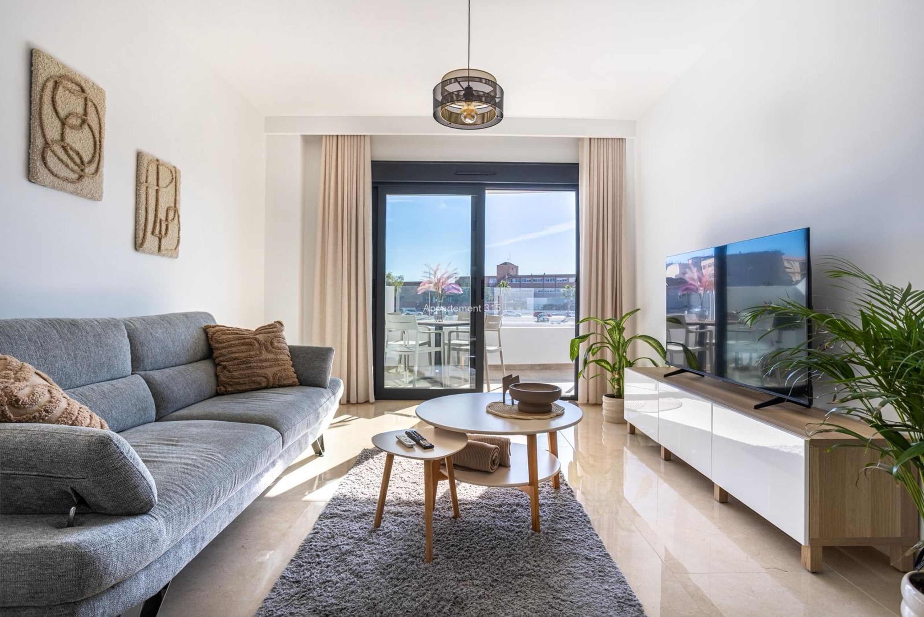 A modern living room with a sofa, a small table, a TV, and a balcony view.