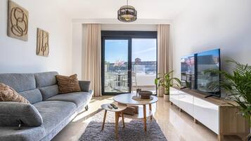 A modern living room with a sofa, a small table, a TV, and a balcony view.