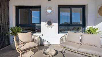 A sunlit outdoor seating area with two wicker chairs and a round table, a decorative mirror, and a potted plant.