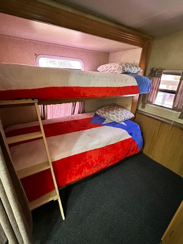 Una cama litera con escalera, una ventana y un estante pequeño con almohadas.