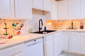 A kitchen with white cabinetry, a black sink, and a marble backsplash. - Nanny`s Nest - A Gentle Place to Land (Nederland)