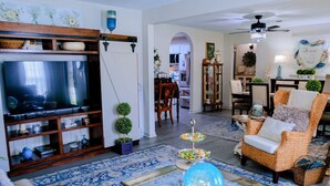 Sala de estar com televisão, mesa de centro, poltrona de vime e tapete estampado.