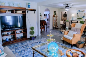 A living room with a television, a coffee table, a wicker armchair, and a patterned rug. - Nanny`s Nest - A Gentle Place to Land (Nederland)