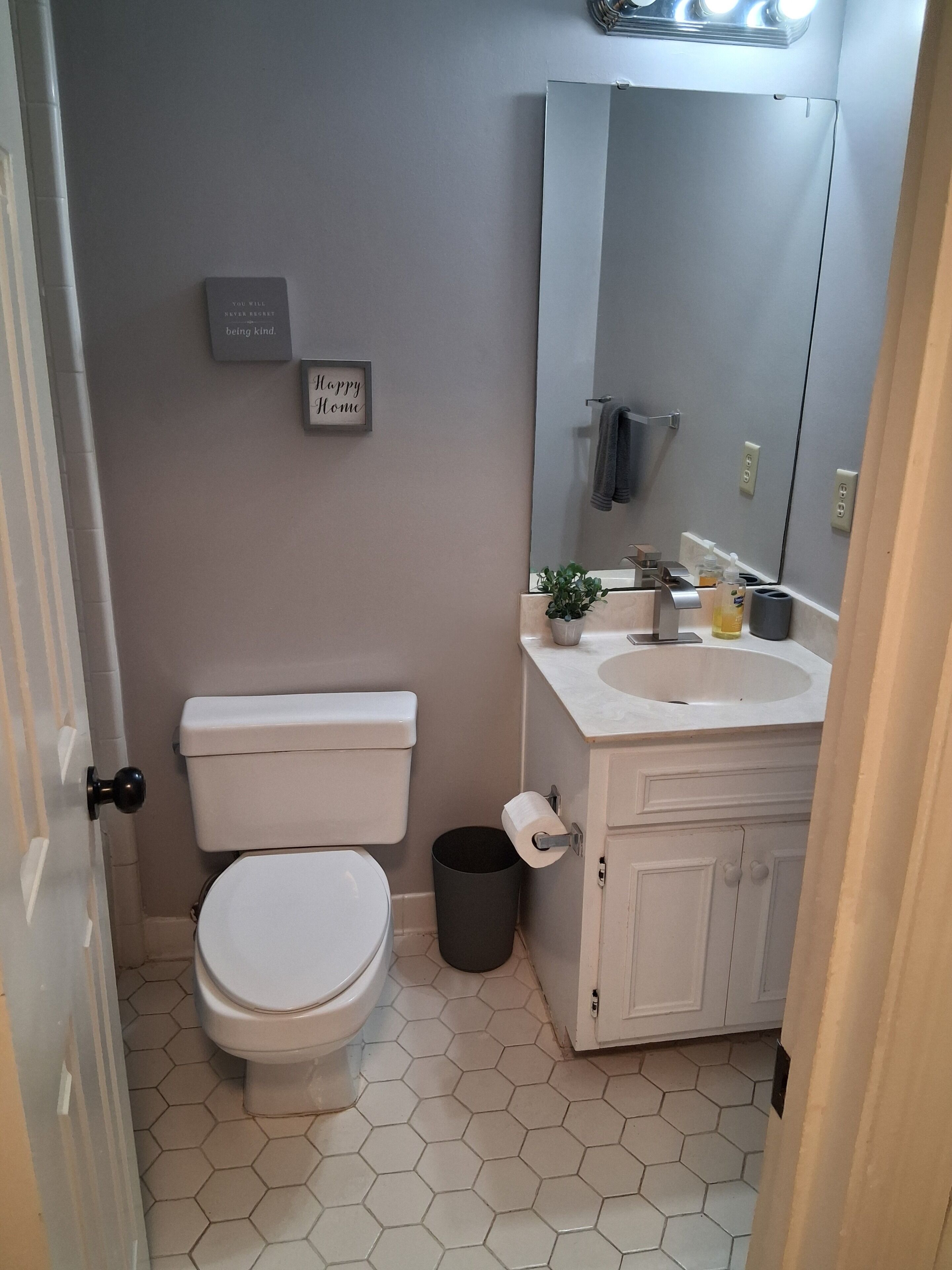 A bathroom with a toilet, sink, mirror, and a trash can.