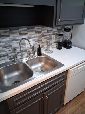 A kitchen with a double sink, a built-in dishwasher, a blender, and a tiled backsplash. - Hidden Gem Townhouse 2-bedroom Flat (Columbus)