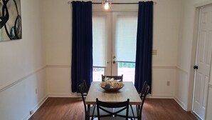 A dining area with a wooden table, four chairs, a bowl, and a ceiling light fixture.
