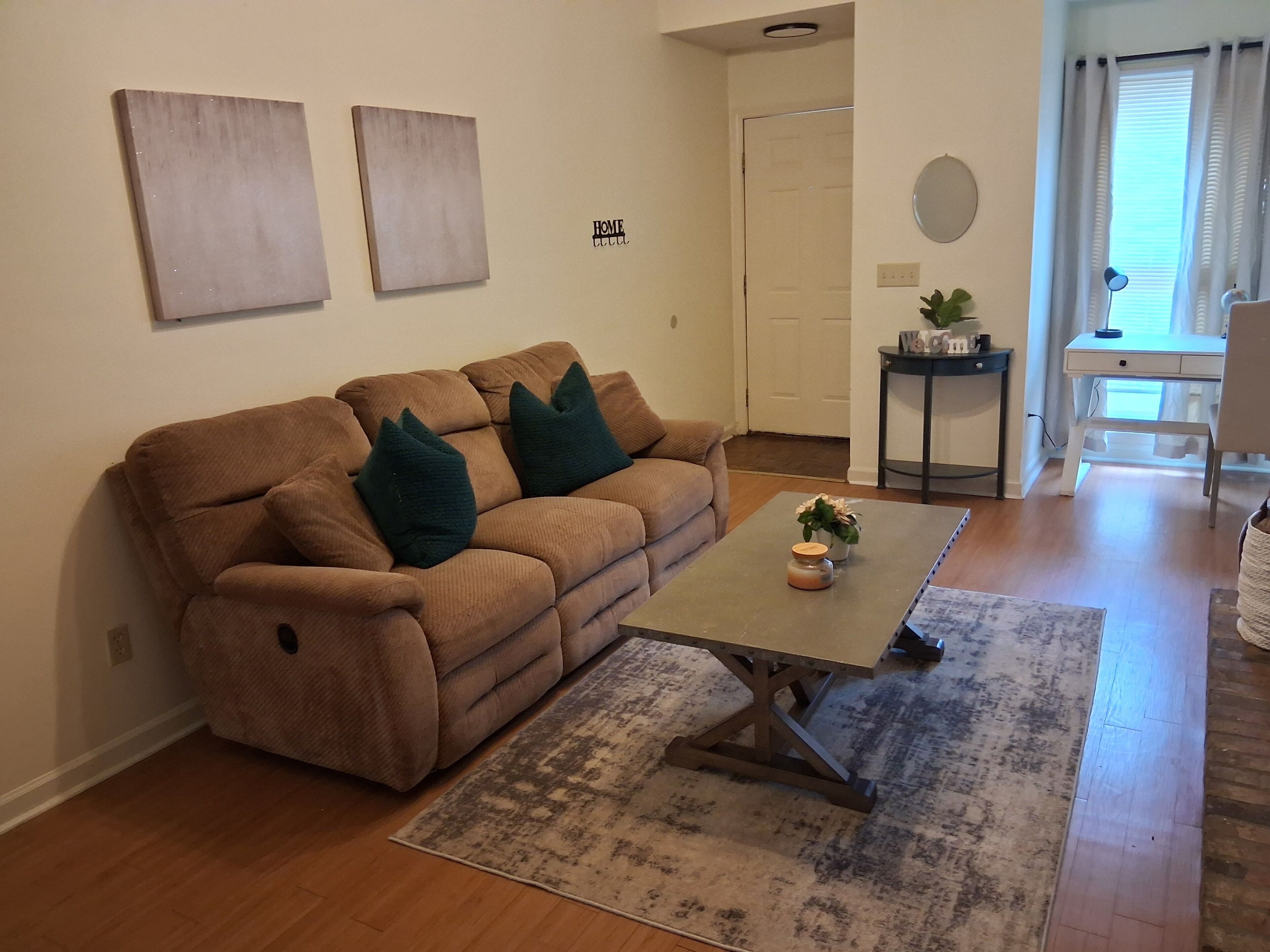 Un salon avec un canapé marron, deux coussins verts, une table basse et un tapis.