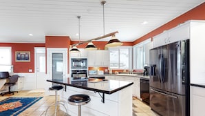 Una cocina moderna con armarios blancos, un refrigerador de acero inoxidable grande y una isla central con taburetes de bar.