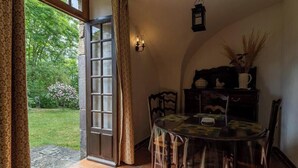 Ein Essbereich mit Tisch, Stühlen, einer Lampe und Blick auf einen Garten durch eine offene Tür.