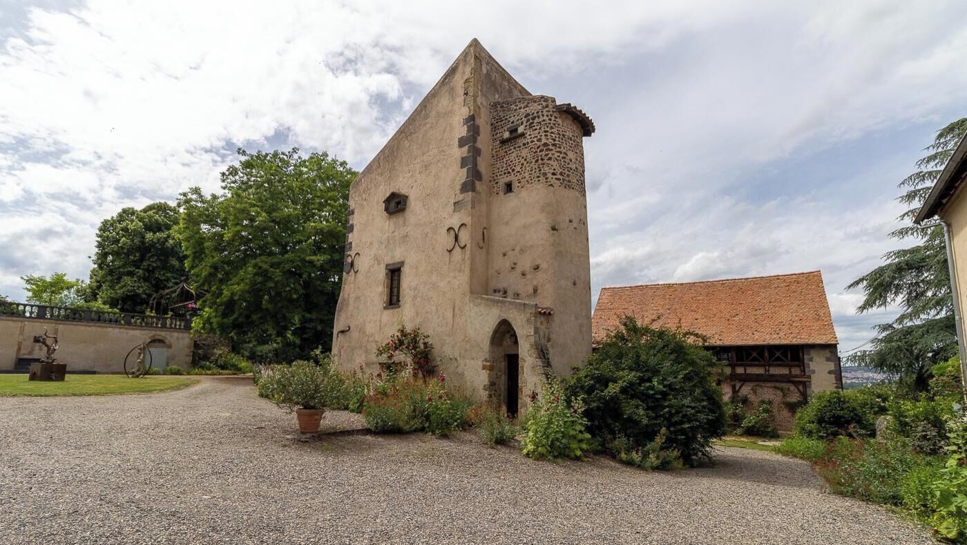 A historic stone building with a tower, surrounded by gravel paths and greenery.