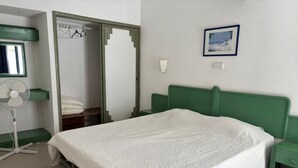 A bedroom with a single bed, a green headboard, a nightstand, a bedside table, a wall-mounted fan, a mirror, and a framed picture on the wall. - 1-Bedroom Apartment in Praia da Rocha, Porimão (Portimão)