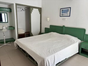 A bedroom with a single bed, a green headboard, a nightstand, a bedside table, a wall-mounted fan, a mirror, and a framed picture on the wall. - 1-Bedroom Apartment in Praia da Rocha, Porimão (Portimão)