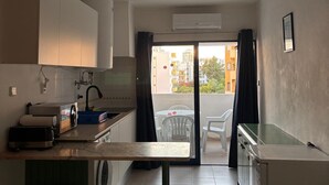 A compact kitchen with a washing machine, a small dining area, and a view of buildings through a glass door. - 1-Bedroom Apartment in Praia da Rocha, Porimão (Portimão)