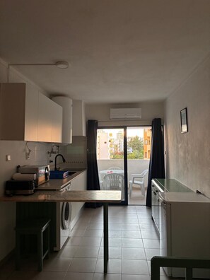A compact kitchen with a washing machine, a small dining area, and a view of buildings through a glass door. - 1-Bedroom Apartment in Praia da Rocha, Porimão (Portimão)