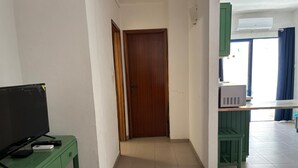 A room with a television on a green desk, a wooden door, and a kitchenette with a microwave. - 1-Bedroom Apartment in Praia da Rocha, Porimão (Portimão)