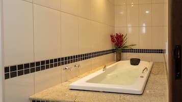 A bathroom with a bathtub, a sink, and a toilet. There is a towel on the floor and a flower vase on the counter.