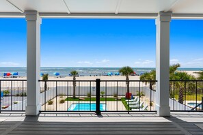 A balcony with a view of a beach, a pool, and a fenced area with umbrellas. - Sea Dreams- Ocean Isle Beach (Ocean Isle Beach)