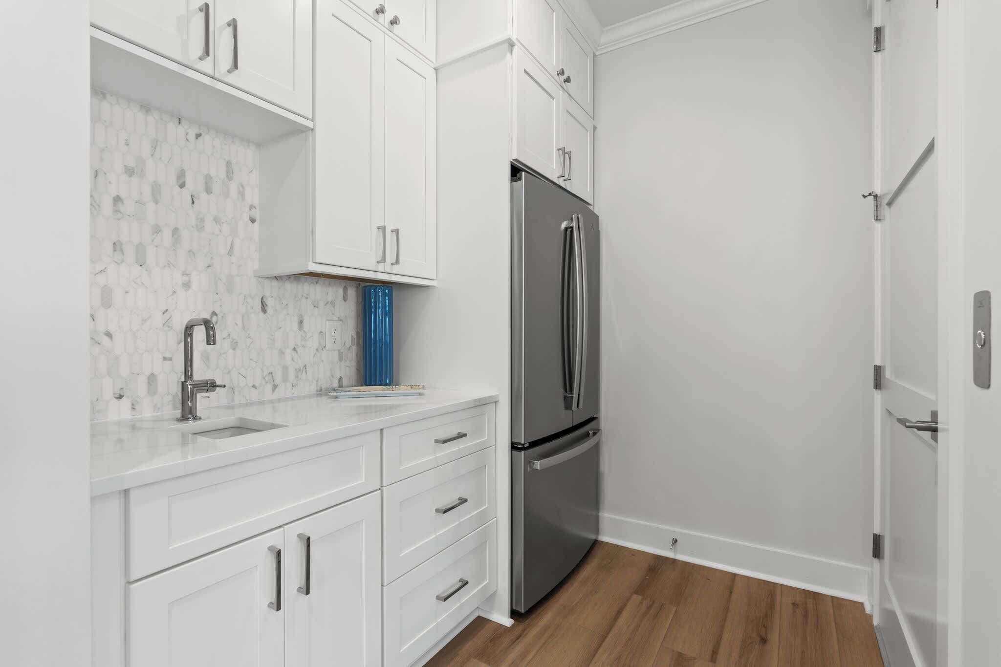 Una cocina moderna con armarios blancos, un refrigerador de acero inoxidable y una salpicadura de mármol.
