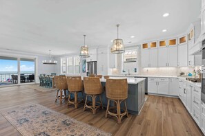 A modern kitchen with white cabinets, a central island, bar stools, and pendant lighting. - Sea Dreams- Ocean Isle Beach (Ocean Isle Beach)