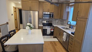 A modern kitchen with wooden cabinets, stainless steel appliances, a central island, and a dining area with chairs. - Perfect Luxury 4-bedroom house with Central AC in Rochester (Rochester)