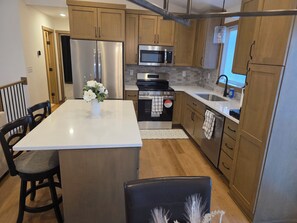 A modern kitchen with wooden cabinets, stainless steel appliances, a central island, and a dining area with chairs. - Perfect Luxury 4-bedroom house with Central AC in Rochester (Rochester)