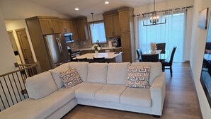 A modern living room with a sectional sofa, wooden flooring, and a kitchen in the background. - Perfect Luxury 4-bedroom house with Central AC in Rochester (Rochester)