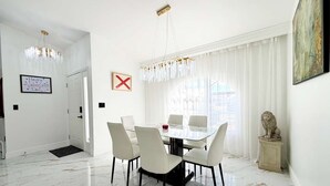 A dining area with a glass table and chairs, a chandelier, a white door, and a framed picture on the wall. - Designer house near Disney with private pool, water views, and custom pool table (Kissimmee)