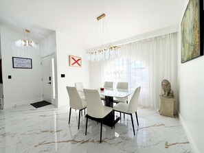 A dining area with a glass table and chairs, a chandelier, a white door, and a framed picture on the wall. - Designer house near Disney with private pool, water views, and custom pool table (Kissimmee)