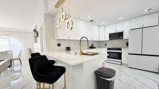 A modern kitchen with white cabinetry, a marble countertop, and a black trash bin. - Designer house near Disney with private pool, water views, and custom pool table (Kissimmee)