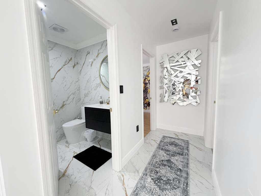 Un pasillo con suelo de mármol, alfombra negra, inodoro blanco, tocador negro y una pared decorada con una obra de arte geométrica.