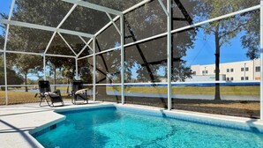 A swimming pool with a clear blue water, surrounded by a white metal structure, and two lounge chairs. - Designer house near Disney with private pool, water views, and custom pool table (Kissimmee)