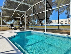 Ein Swimmingpool mit klarem, blauem Wasser, umgeben von einer weißen Metallkonstruktion und zwei Liegestühlen.