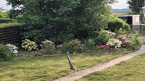 Um jardim com caminho pavimentado, vegetação exuberante e plantas floridas.