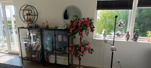Ein Zimmer mit einem Glasvitrine, einem Spiegel, einer Topfpflanze und einem Fenster mit Blick auf Grün.