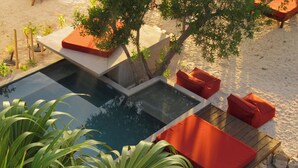 Zona de piscina con terraza de madera, cojines rojos y piscina transparente.