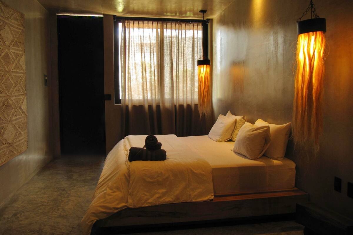 Un dormitorio con cama, cortinas y lámpara colgante.
