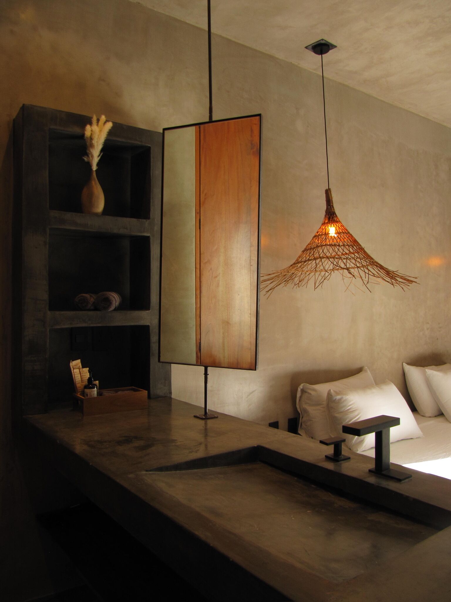 A modern room with a wooden cabinet, a hanging light fixture, and a bed with pillows.