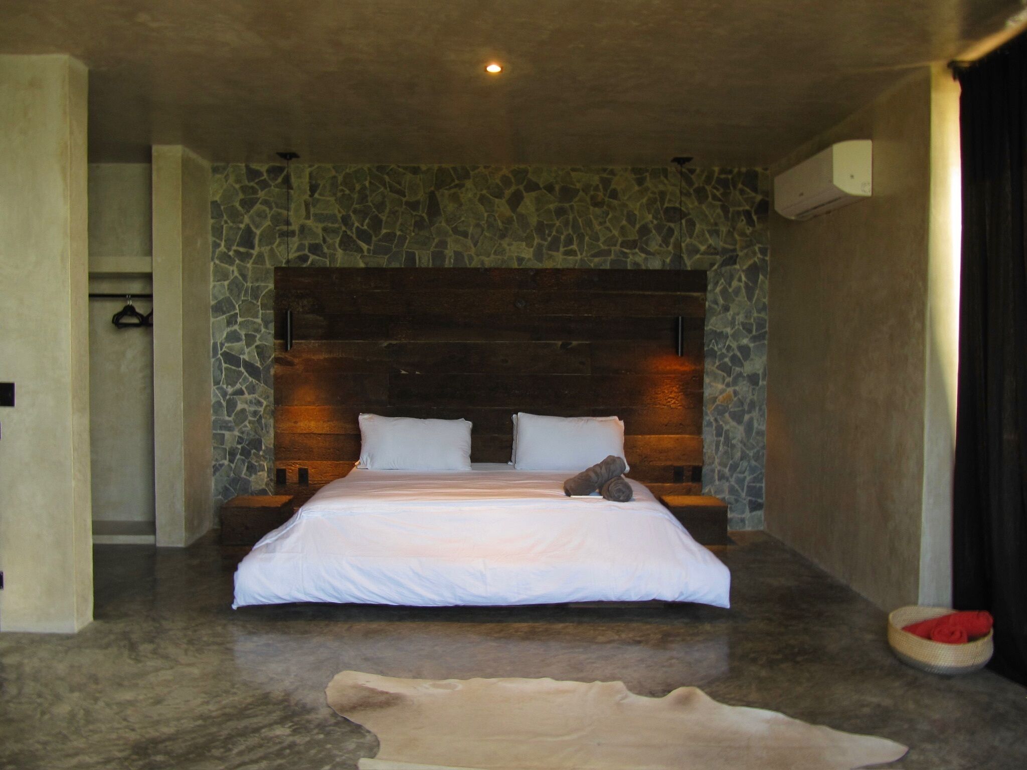Un dormitorio con pared de piedra, cabecera de madera, cama con ropa de cama blanca y una alfombra pequeña.