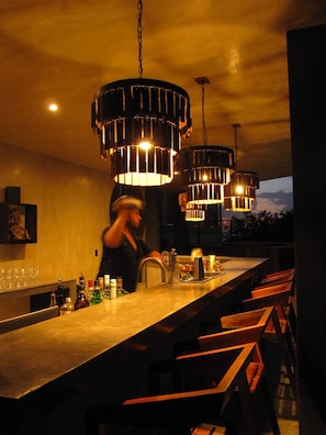 A bar area with a long counter, hanging pendant lights, and a view of the sky. - Hotel Amadeo (Isla Holbox)